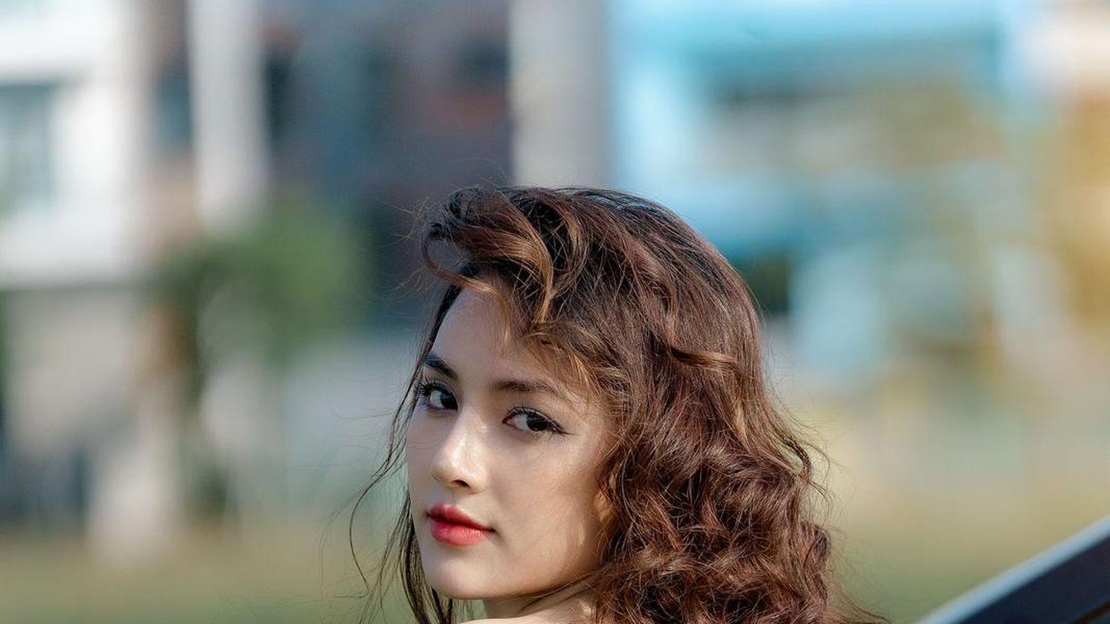A woman leaning against a car in an evening dress