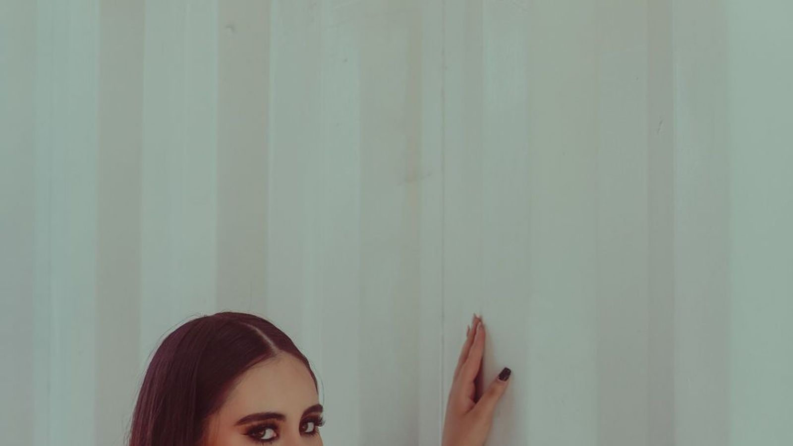 A close-up portrait of a woman against a plain wall