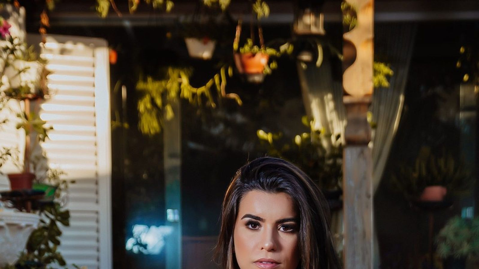 A woman in a black dress resting against a stool on a patio