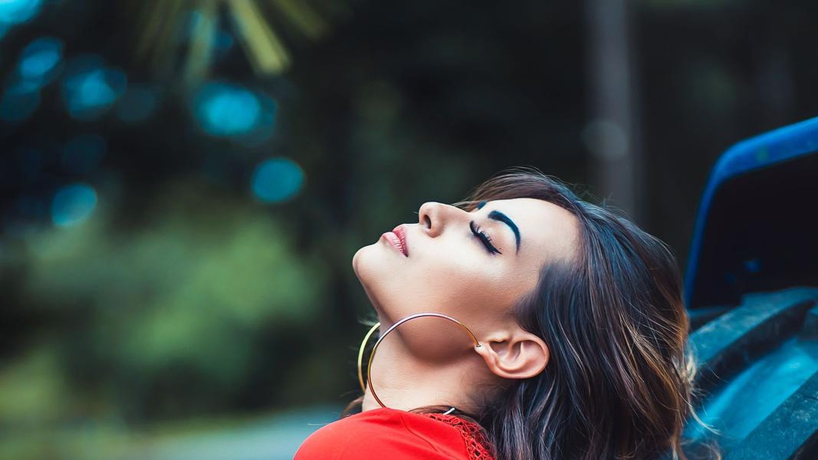 A woman in a red top outdoors, leaning against a truck tire